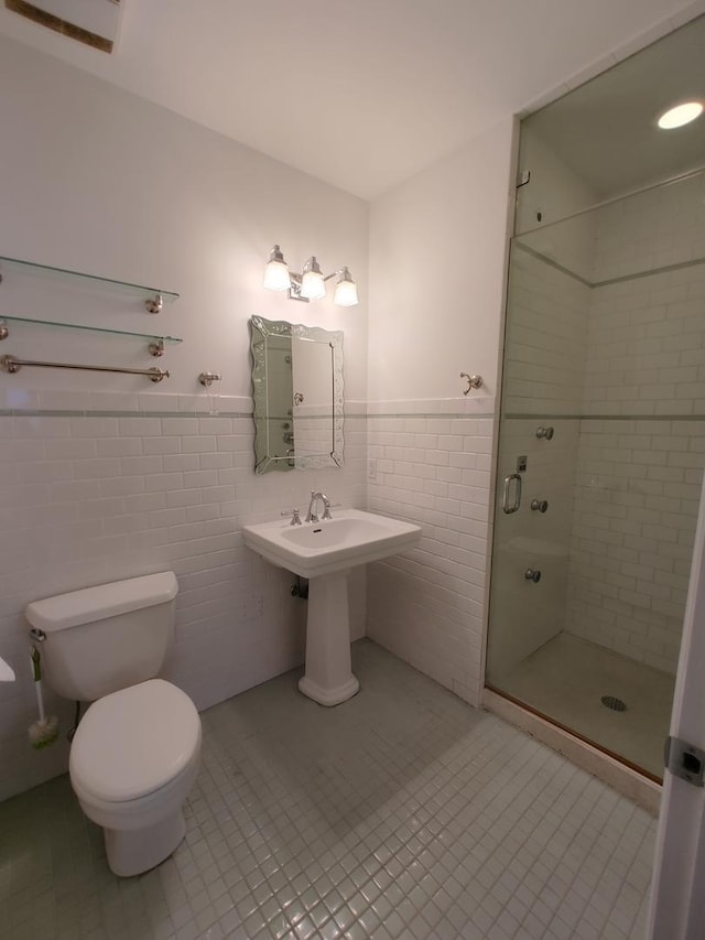 bathroom with a shower with door, tile patterned flooring, tile walls, and toilet