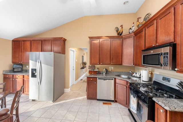 kitchen with vaulted ceiling, appliances with stainless steel finishes, sink, light tile patterned floors, and light stone counters