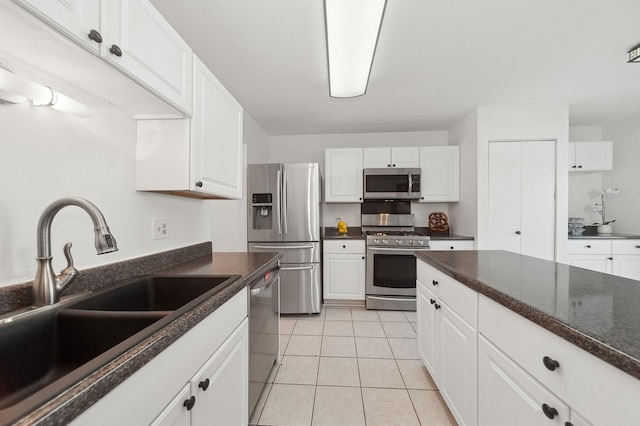 kitchen with appliances with stainless steel finishes, white cabinetry, a sink, and light tile patterned floors