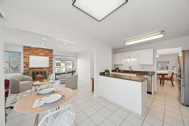 kitchen featuring light tile patterned floors, white cabinets, appliances with stainless steel finishes, a brick fireplace, and dark countertops