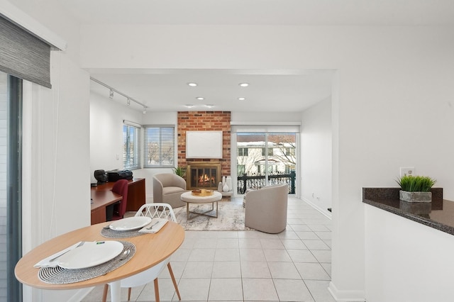 living area with light tile patterned floors, recessed lighting, rail lighting, a brick fireplace, and baseboards