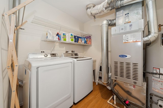 clothes washing area with light wood-type flooring, laundry area, strapped water heater, and washing machine and clothes dryer