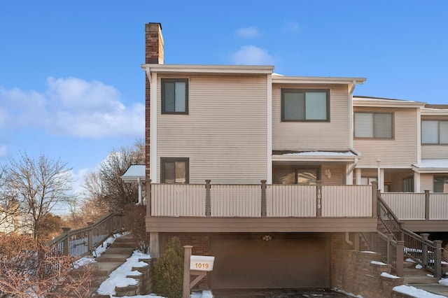 back of property featuring a balcony, an attached garage, a chimney, and stairway