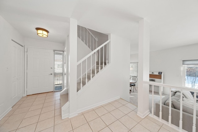 entrance foyer featuring light tile patterned floors, baseboards, and stairway