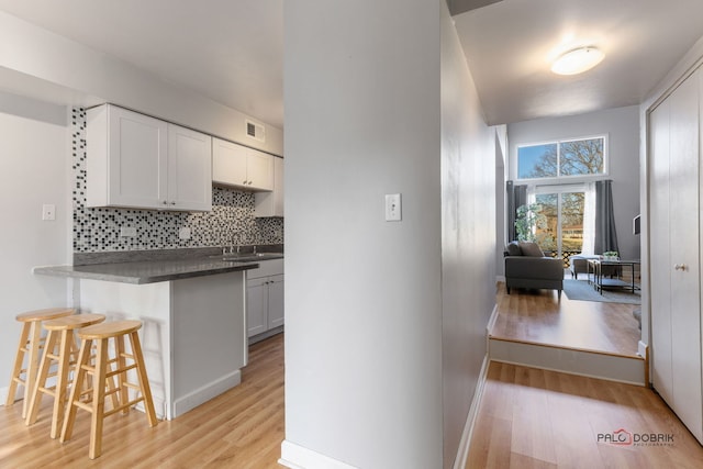 kitchen featuring white cabinetry, a kitchen breakfast bar, tasteful backsplash, and light wood-type flooring