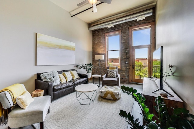 living room with a towering ceiling, ceiling fan, and brick wall