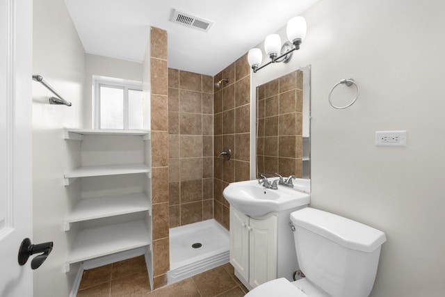 bathroom with tile patterned flooring, vanity, tiled shower, and toilet