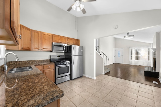 kitchen with sink, light tile patterned floors, dark stone countertops, stainless steel appliances, and vaulted ceiling