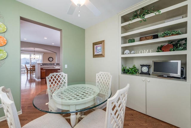 dining room with hardwood / wood-style flooring, ceiling fan with notable chandelier, and built in features