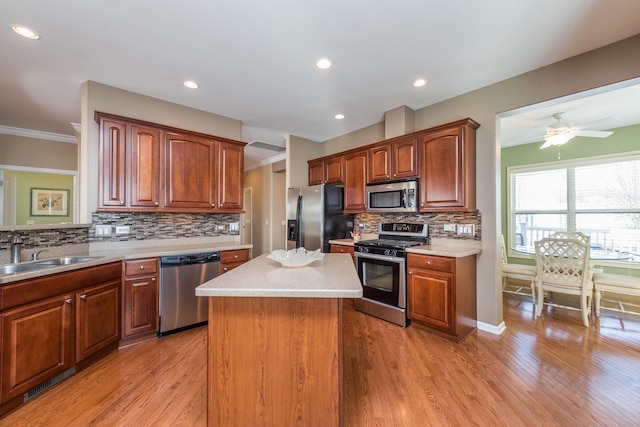 kitchen with a kitchen island, appliances with stainless steel finishes, sink, light hardwood / wood-style floors, and crown molding