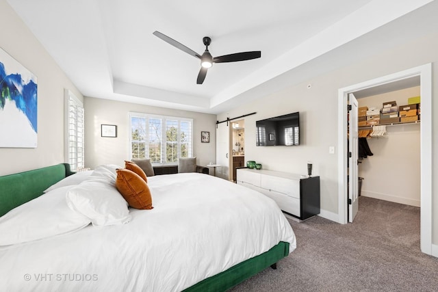 bedroom featuring a barn door, baseboards, a tray ceiling, a walk in closet, and carpet floors