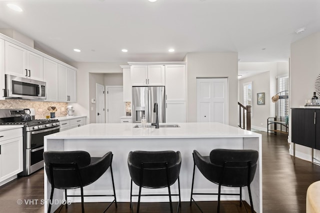 kitchen featuring a sink, appliances with stainless steel finishes, tasteful backsplash, a kitchen bar, and a center island with sink