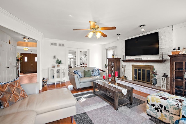 living room featuring crown molding, a brick fireplace, light hardwood / wood-style flooring, and french doors