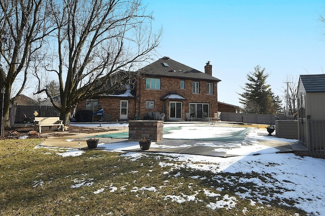 snow covered rear of property with a patio and a covered pool