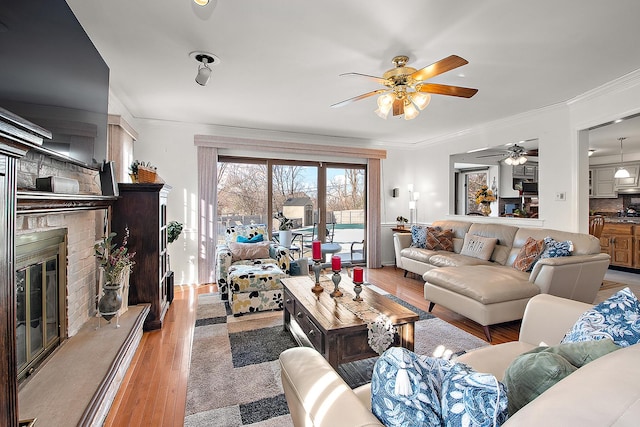 living room featuring ornamental molding, ceiling fan, a fireplace, and light hardwood / wood-style flooring