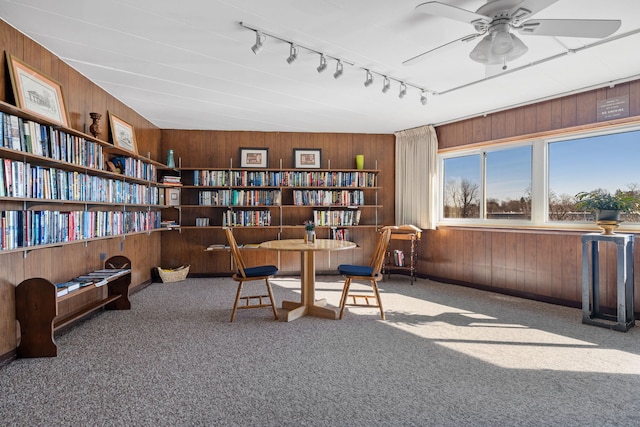 living area with ceiling fan, carpet flooring, track lighting, and wooden walls