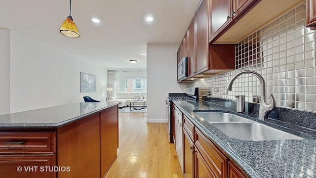 kitchen with sink, dark stone countertops, appliances with stainless steel finishes, pendant lighting, and light hardwood / wood-style floors