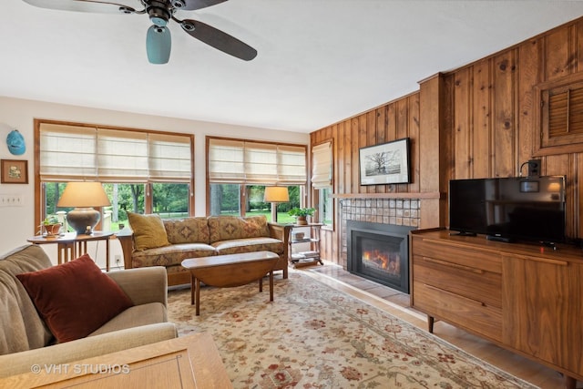 living room with ceiling fan, a fireplace, wooden walls, and light hardwood / wood-style floors