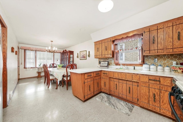 kitchen featuring range with gas cooktop, decorative light fixtures, sink, backsplash, and kitchen peninsula