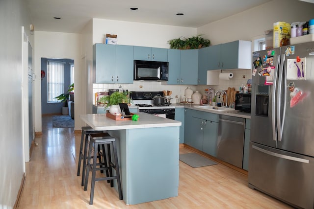 kitchen with appliances with stainless steel finishes, a kitchen breakfast bar, a center island, tasteful backsplash, and blue cabinets