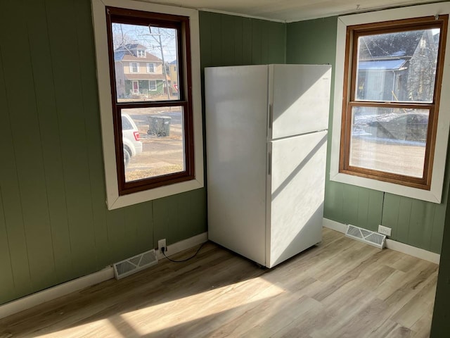 unfurnished bedroom with wooden walls, light hardwood / wood-style floors, and white fridge