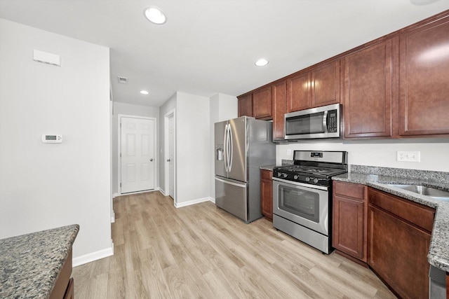 kitchen featuring dark stone countertops, sink, light hardwood / wood-style flooring, and appliances with stainless steel finishes