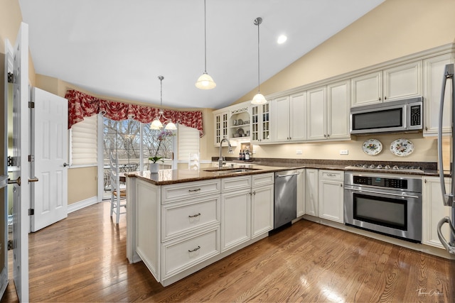 kitchen featuring appliances with stainless steel finishes, decorative light fixtures, sink, dark stone counters, and light hardwood / wood-style floors