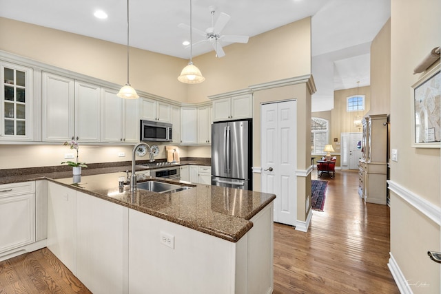 kitchen featuring appliances with stainless steel finishes, white cabinetry, hanging light fixtures, hardwood / wood-style floors, and dark stone countertops