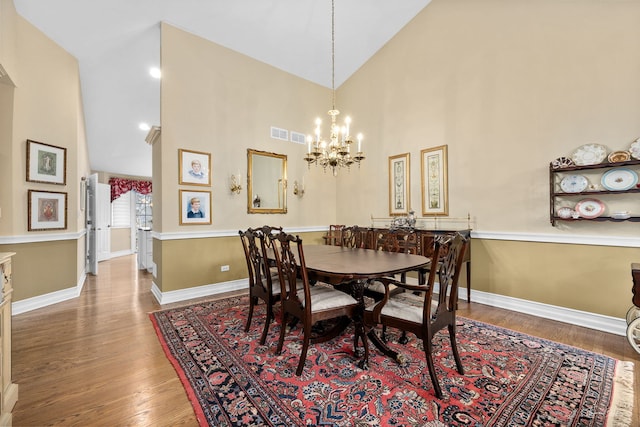 dining space featuring high vaulted ceiling, hardwood / wood-style floors, and an inviting chandelier