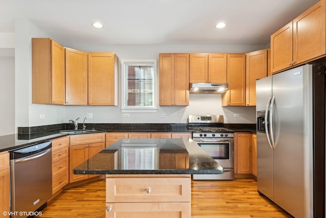 kitchen featuring sink, appliances with stainless steel finishes, dark stone countertops, a kitchen island, and light wood-type flooring