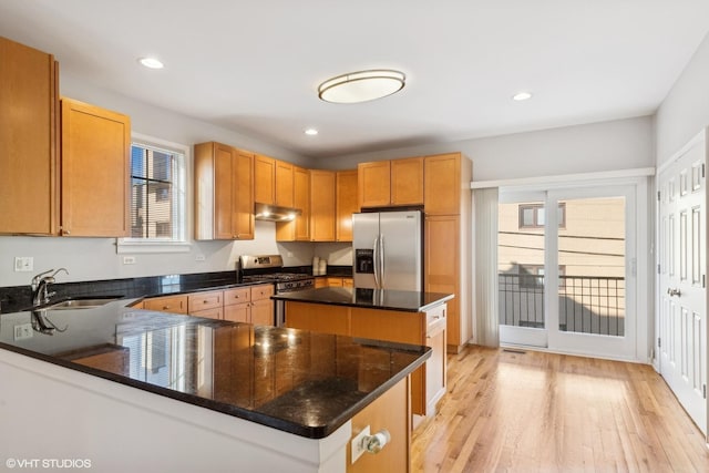 kitchen with a kitchen island, sink, dark stone counters, stainless steel appliances, and light hardwood / wood-style flooring