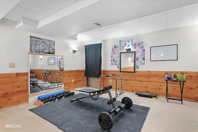 workout room featuring a drop ceiling and wooden walls