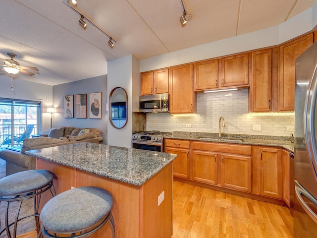 kitchen with brown cabinets, stainless steel appliances, light wood-style flooring, a sink, and dark stone countertops