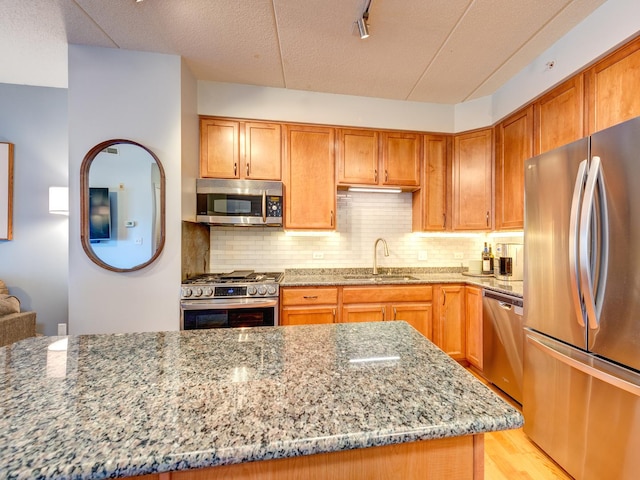 kitchen with appliances with stainless steel finishes, a sink, decorative backsplash, and light stone countertops