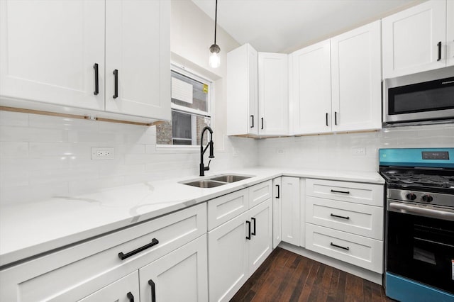 kitchen with appliances with stainless steel finishes, white cabinetry, sink, backsplash, and hanging light fixtures