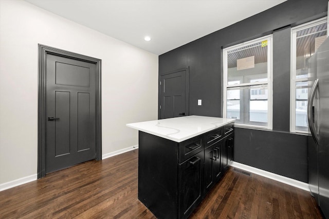 kitchen with dark wood-type flooring, light stone countertops, stainless steel refrigerator, and kitchen peninsula