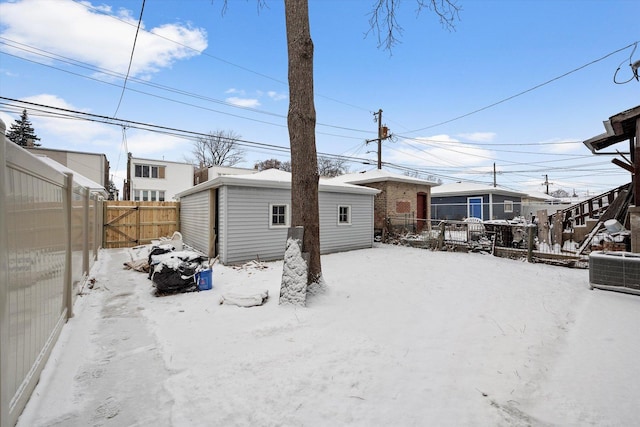 snow covered back of property with central AC unit and an outdoor structure