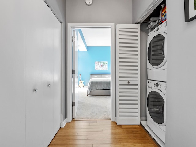 laundry area featuring stacked washer / drying machine and light wood-type flooring