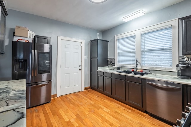 kitchen featuring appliances with stainless steel finishes, light stone countertops, sink, and light wood-type flooring