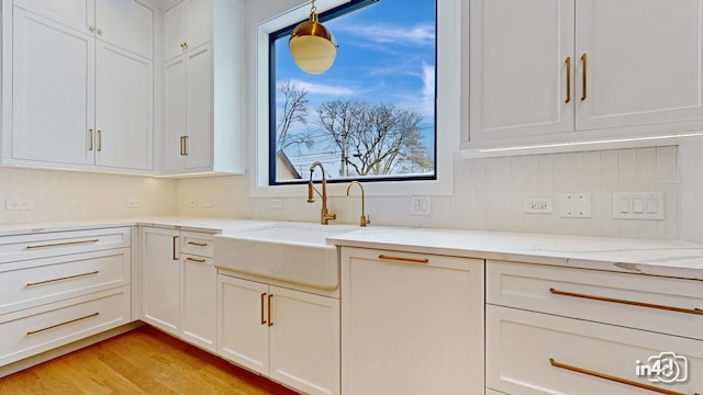 kitchen with sink, hanging light fixtures, light hardwood / wood-style flooring, light stone countertops, and white cabinets