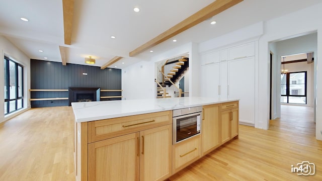 kitchen featuring a spacious island, light brown cabinetry, beam ceiling, and light hardwood / wood-style flooring