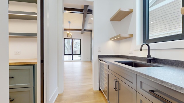 kitchen featuring wine cooler, sink, hanging light fixtures, light hardwood / wood-style flooring, and beam ceiling