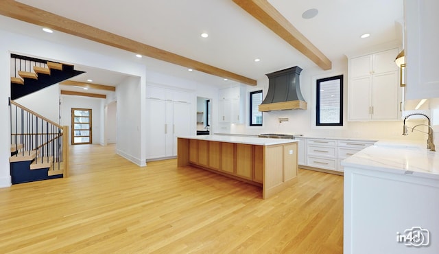 kitchen with premium range hood, white cabinetry, sink, beam ceiling, and a spacious island