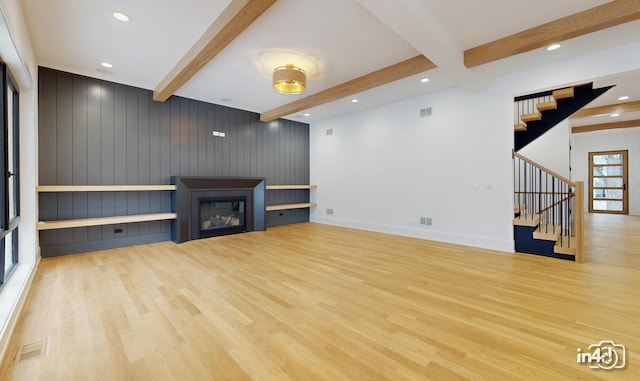 unfurnished living room with wood walls, beamed ceiling, and light wood-type flooring