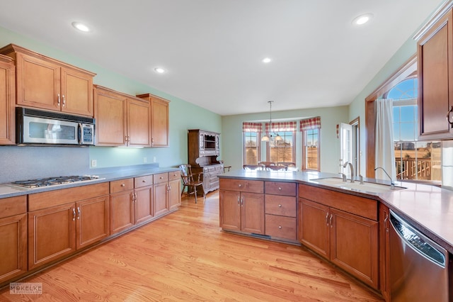 kitchen with appliances with stainless steel finishes, decorative light fixtures, sink, a chandelier, and light hardwood / wood-style flooring