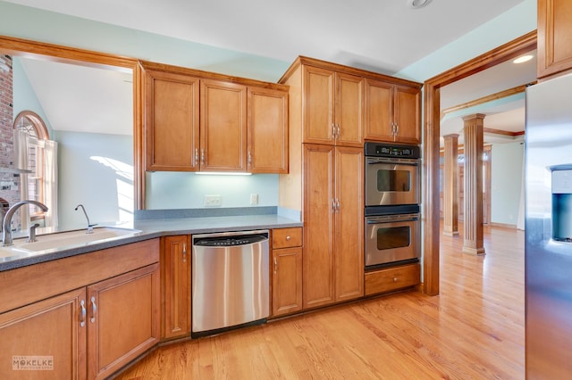 kitchen with stainless steel appliances, sink, decorative columns, and light hardwood / wood-style flooring