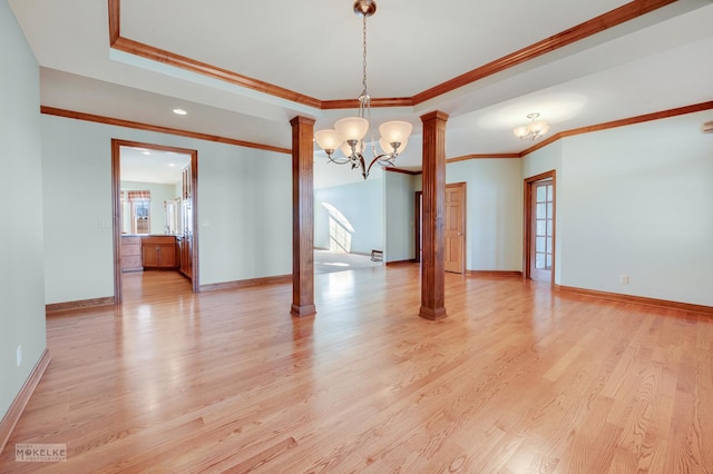 empty room with decorative columns, a chandelier, ornamental molding, a raised ceiling, and light hardwood / wood-style floors