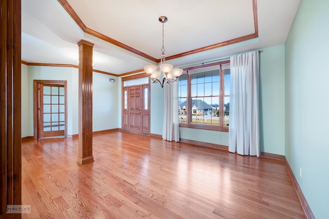 interior space featuring ornate columns, a notable chandelier, light hardwood / wood-style floors, a raised ceiling, and crown molding