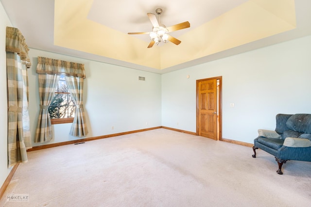 unfurnished room with ceiling fan, a tray ceiling, and light carpet