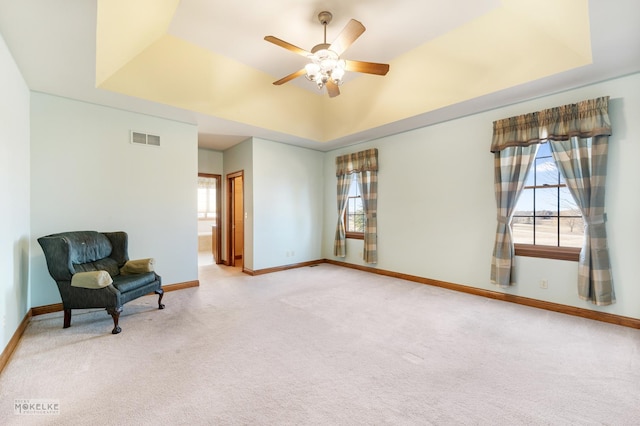 living area with light colored carpet, a raised ceiling, and ceiling fan